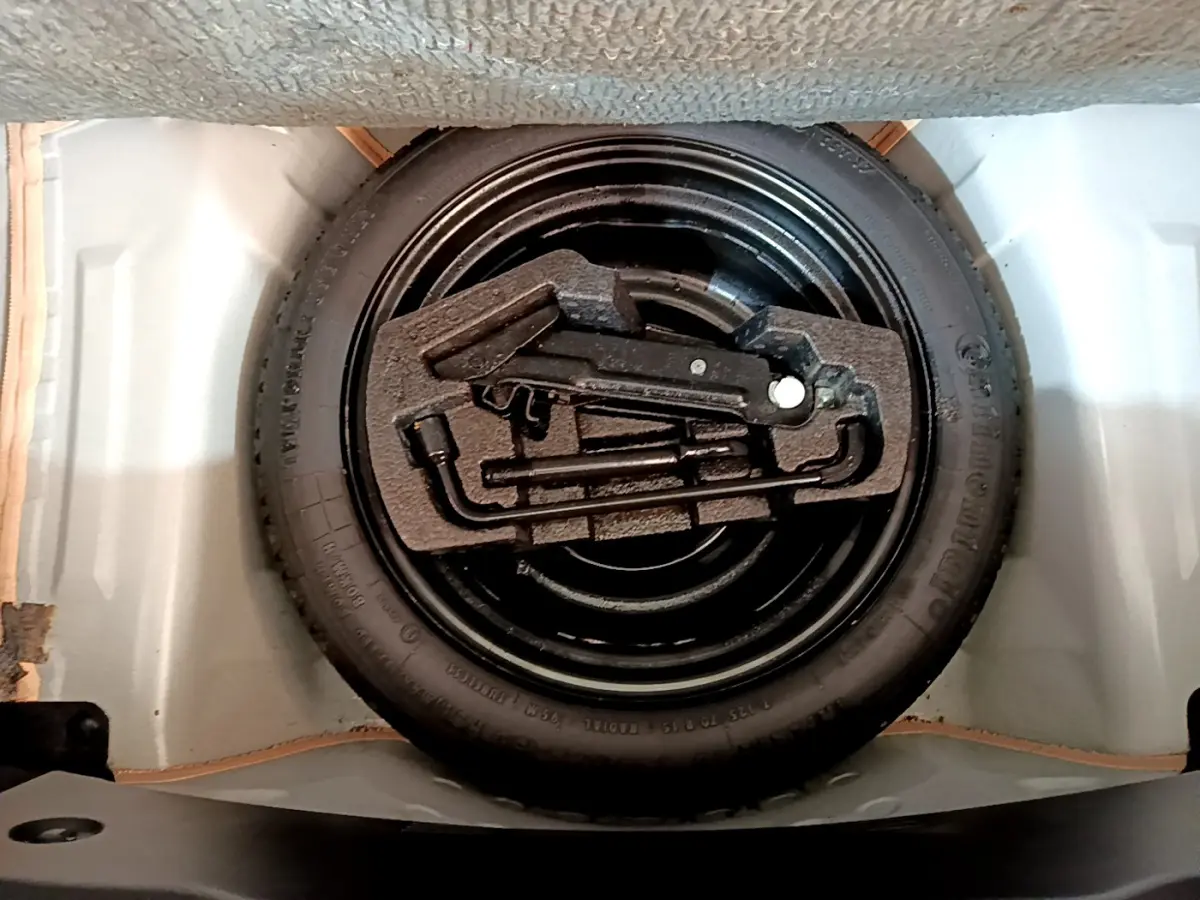 Vue rapprochée de la roue de secours noire avec outils de bord dans le coffre blanc d’une Citroën C1 blanche.