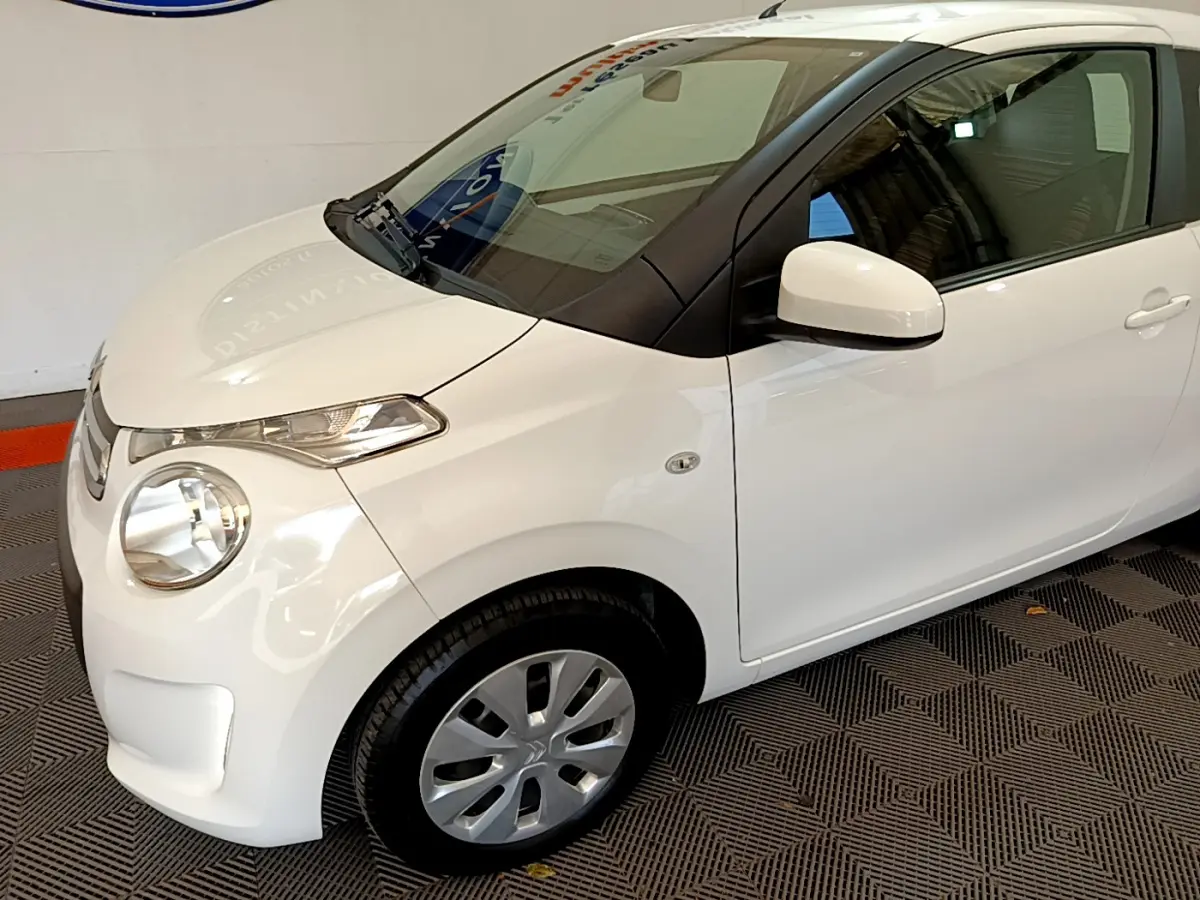 Vue 3/4 avant droit d'une Citroën C1 blanche 2020 avec phares ellipsoïdaux et rétroviseurs peints assortis.