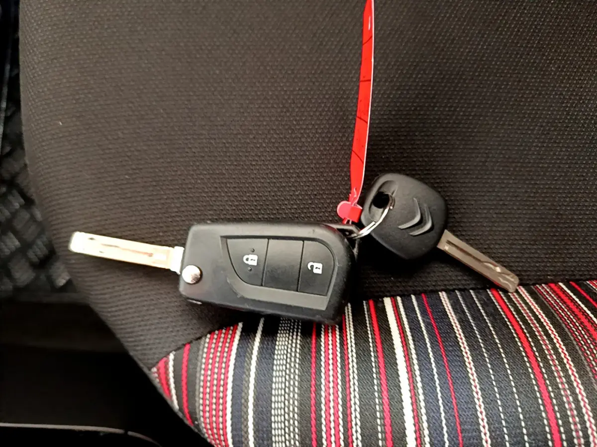 Clé de voiture Citroën posée sur un siège tissu noir à rayures rouges, blanches et grises, intérieur d'une C1 blanche.