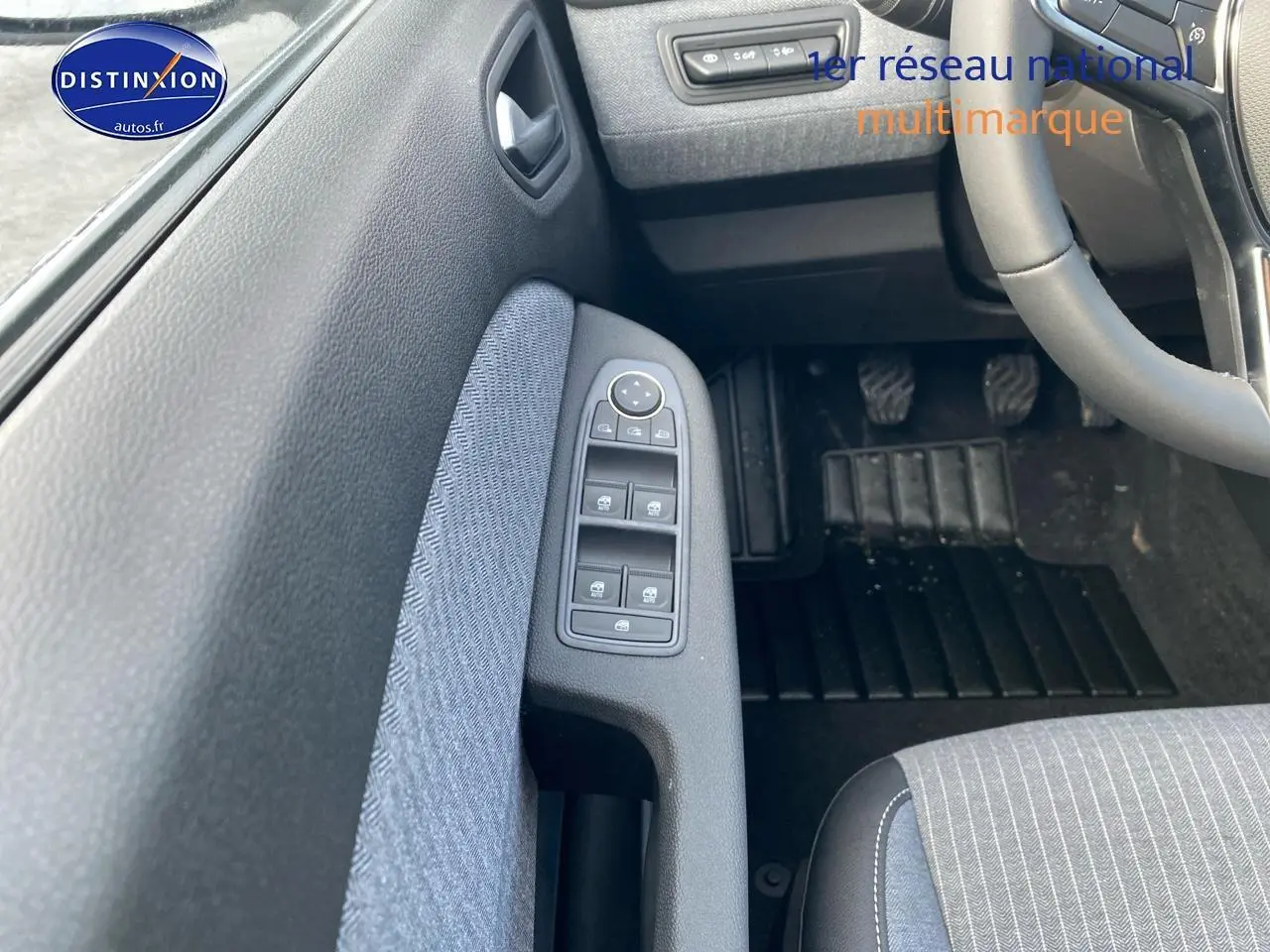 Vue intérieure côté conducteur de la Renault Clio V gris rafale, montrant les commandes des vitres et le pédalier.