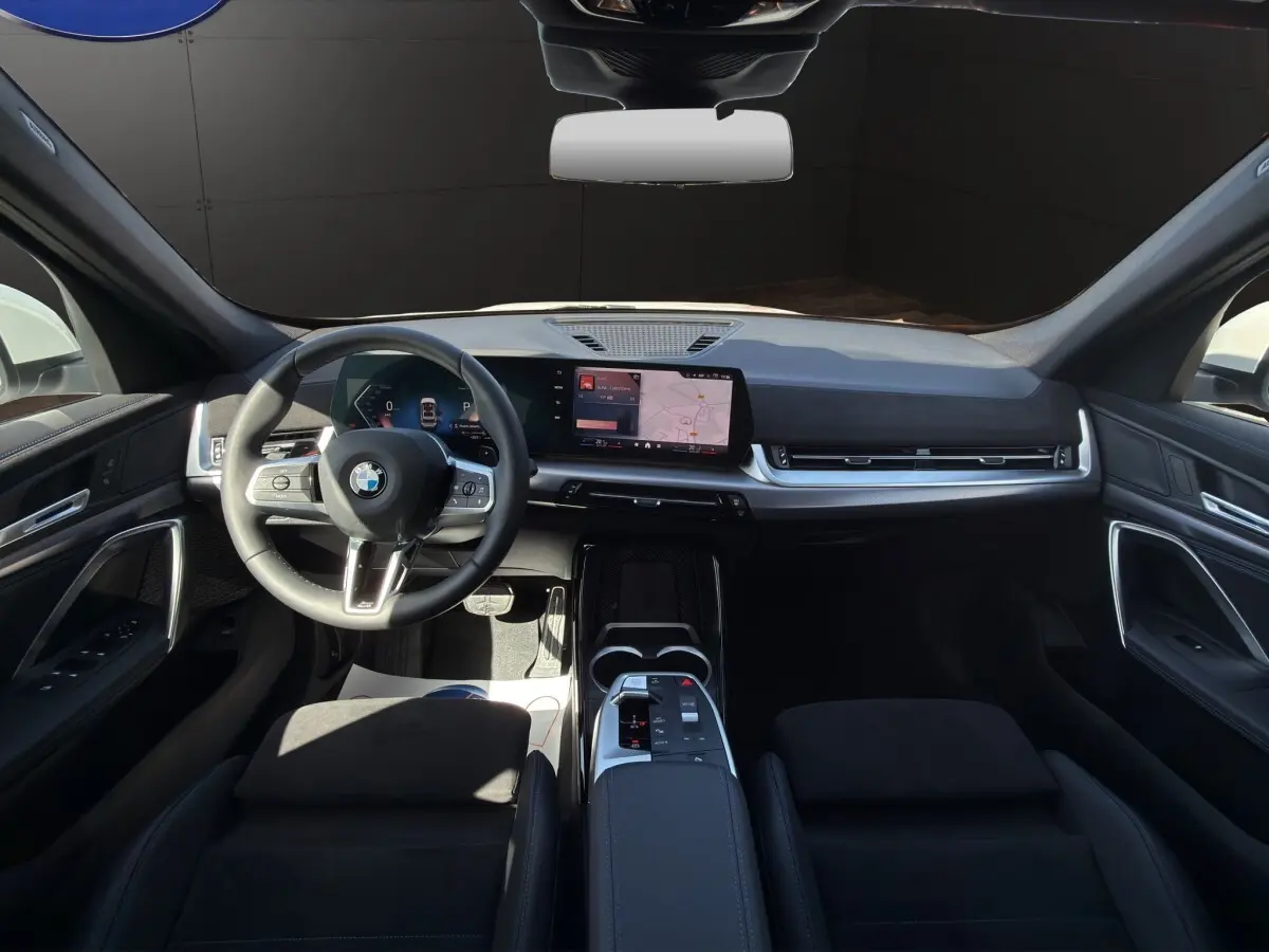 Intérieur noir de la BMW X1 sDrive20d 2025 vu de face, avec tableau de bord numérique et écran tactile central.