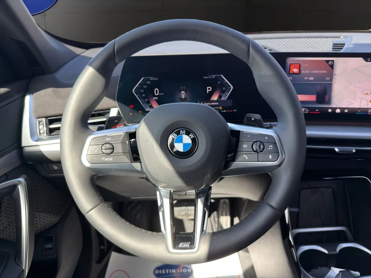 Vue rapprochée du volant noir BMW M Sport avec tableau de bord numérique et écran tactile central.