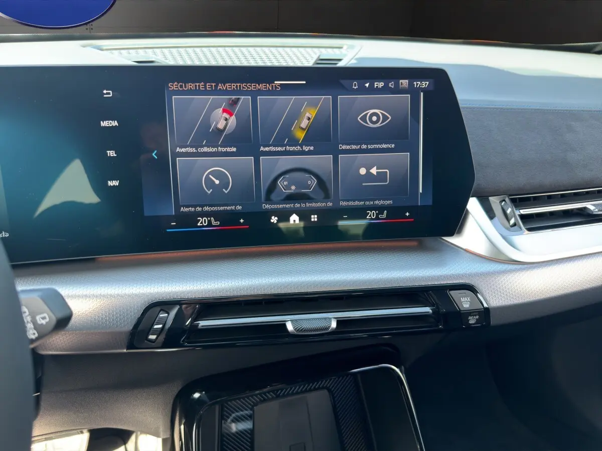 Vue rapprochée de l'écran tactile central du tableau de bord du BMW X1 blanc, affichant les alertes de sécurité.