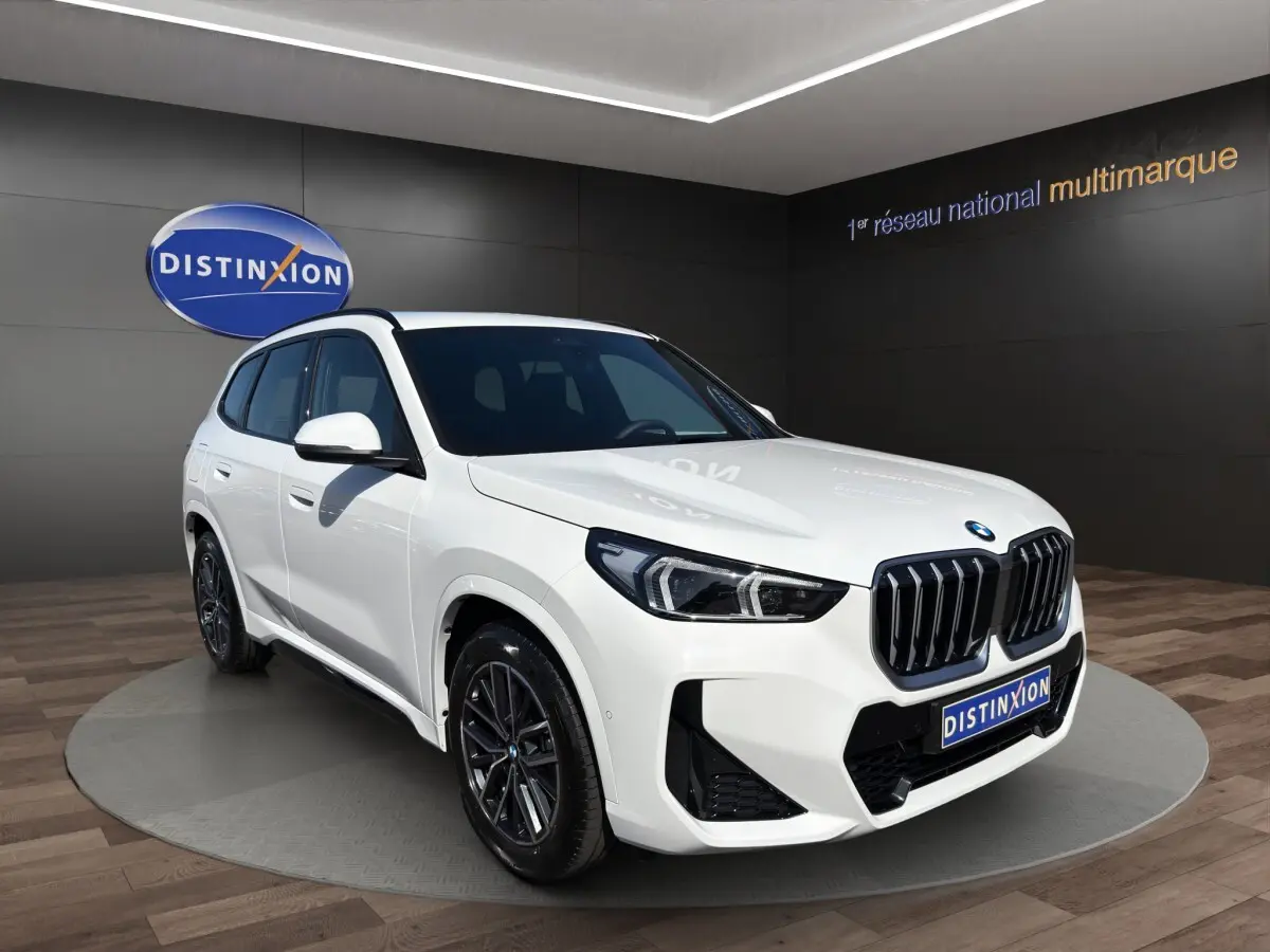 BMW X1 sDrive20d blanc vue 3/4 avant droite avec calandre noire et jantes foncées en showroom
