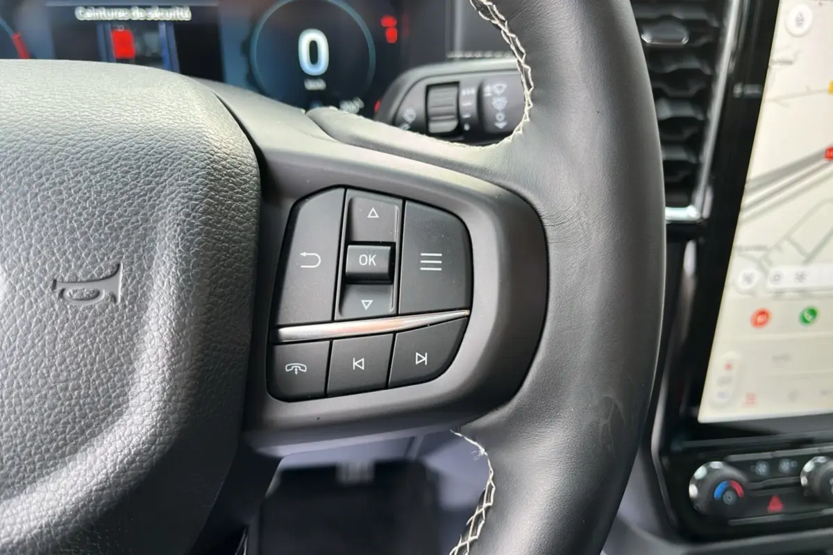 Gros plan sur les commandes au volant cuir noir du Ford Ranger 2026, avec écran tactile et tableau de bord numérique en arrière-plan.
