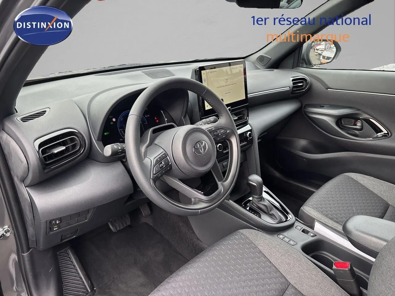 Vue intérieure côté conducteur de la Toyota Yaris Cross gris atlas, avec volant multifonction et écran tactile central.
