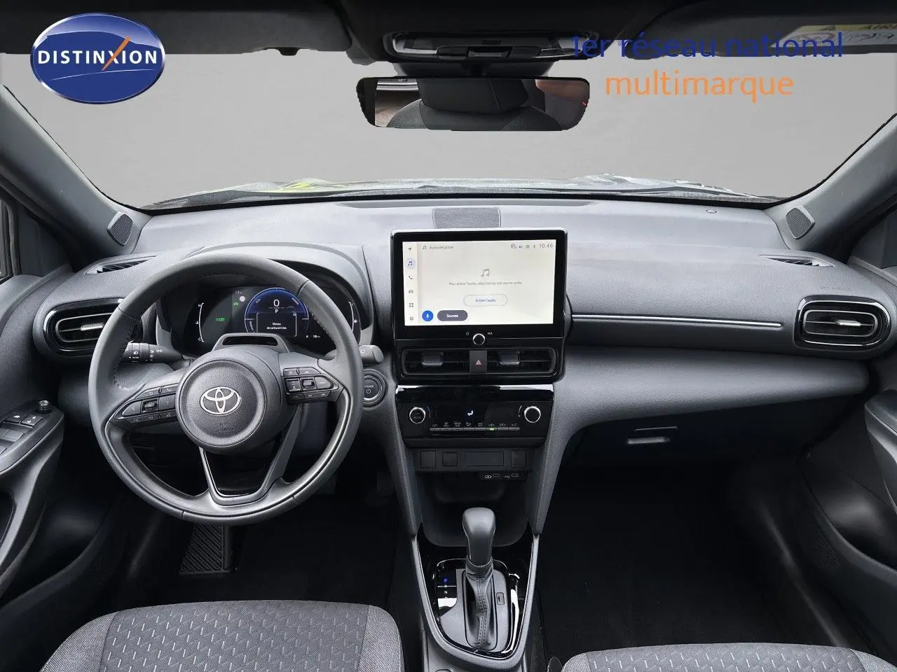 Vue intérieure avant de la Toyota Yaris Cross 1.5 Hybrid, tableau de bord noir avec écran tactile central et volant multifonction.