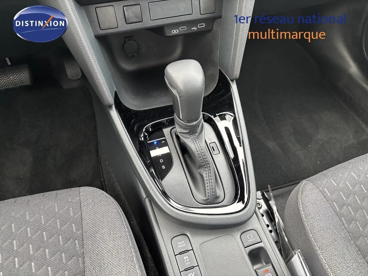 Gros plan sur la console centrale de la Toyota Yaris Cross hybride, mettant en valeur le levier de vitesse automatique et les sièges tissu gris.