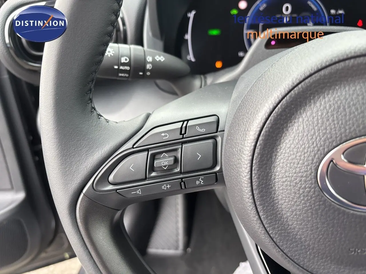 Gros plan sur le volant cuir gris de la Toyota Yaris Cross avec commandes multifonctions et tableau de bord numérique en arrière-plan.