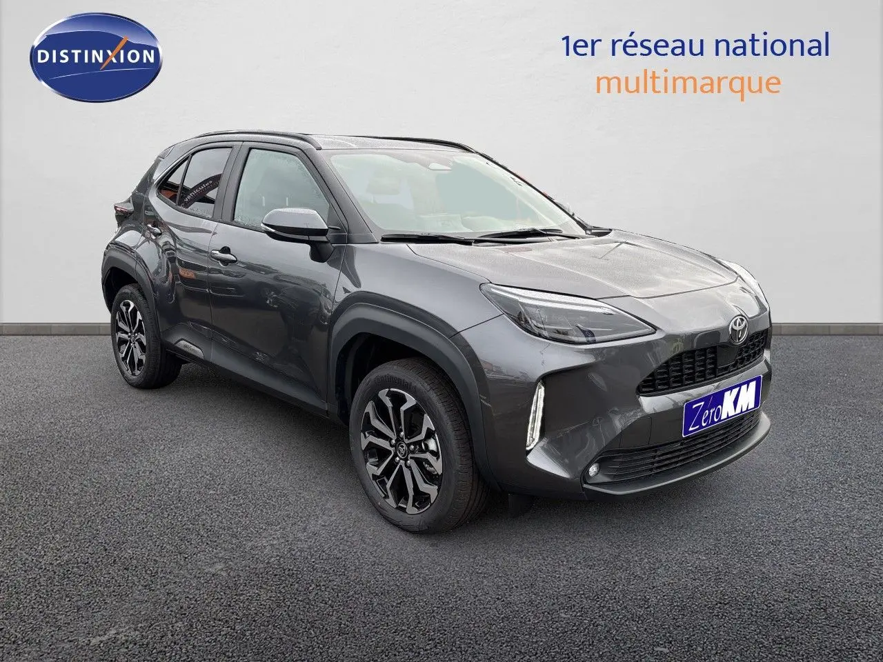 Toyota Yaris Cross gris atlas métal vue 3/4 avant droit avec jantes noires et feux LED allumés.