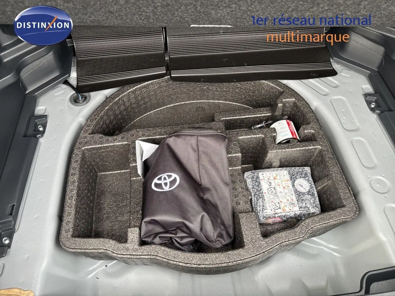 Coffre ouvert d'une Toyota Yaris Cross gris atlas métal, montrant le rangement sous plancher avec kit de secours et accessoires.