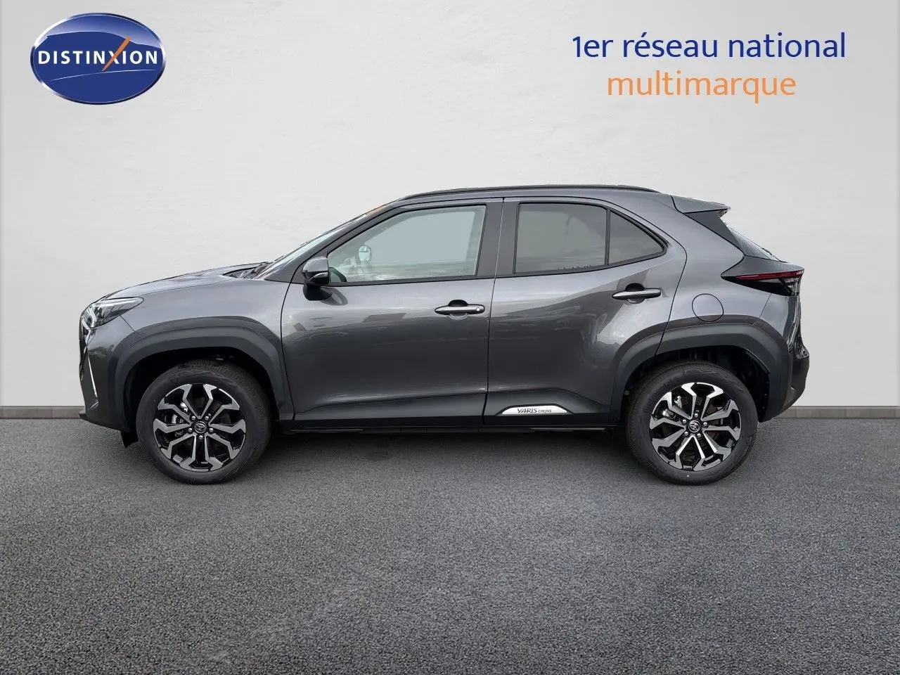 Vue de profil côté gauche d'une Toyota Yaris Cross gris atlas métal avec jantes alliage bicolores et logo sur bas de porte.