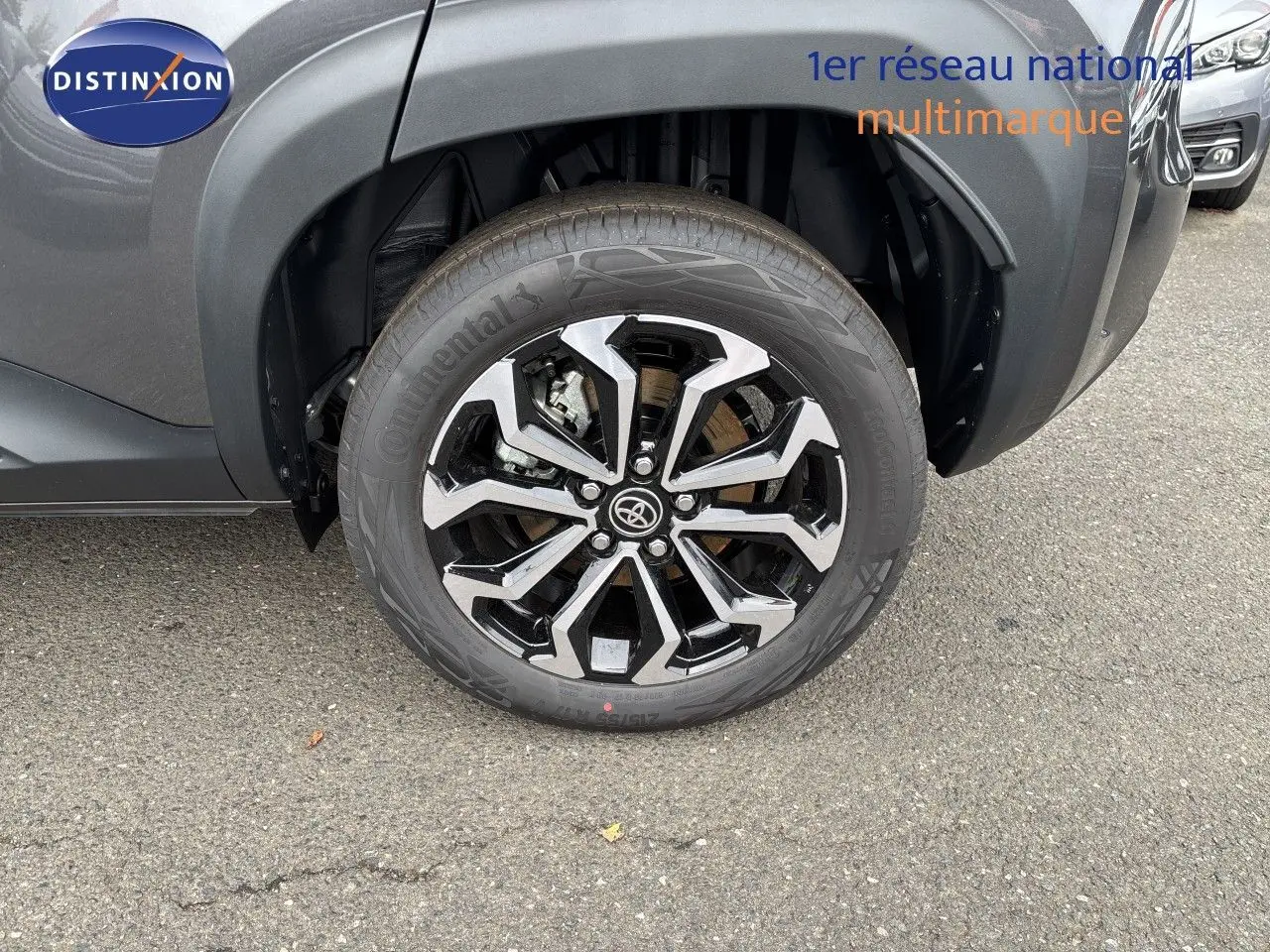 Gros plan sur la roue avant gauche d'une Toyota Yaris Cross gris atlas métal, mettant en valeur la jante alliage bicolore.