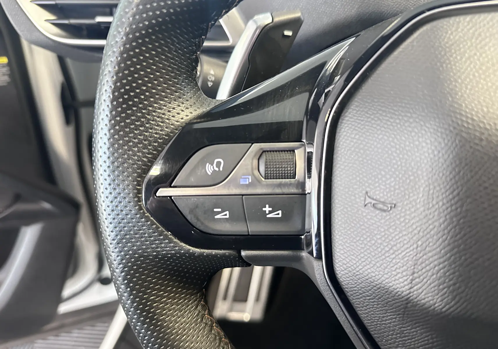 Gros plan sur les commandes du volant en cuir noir du Peugeot 3008 blanc nacré, version 2022, côté gauche.