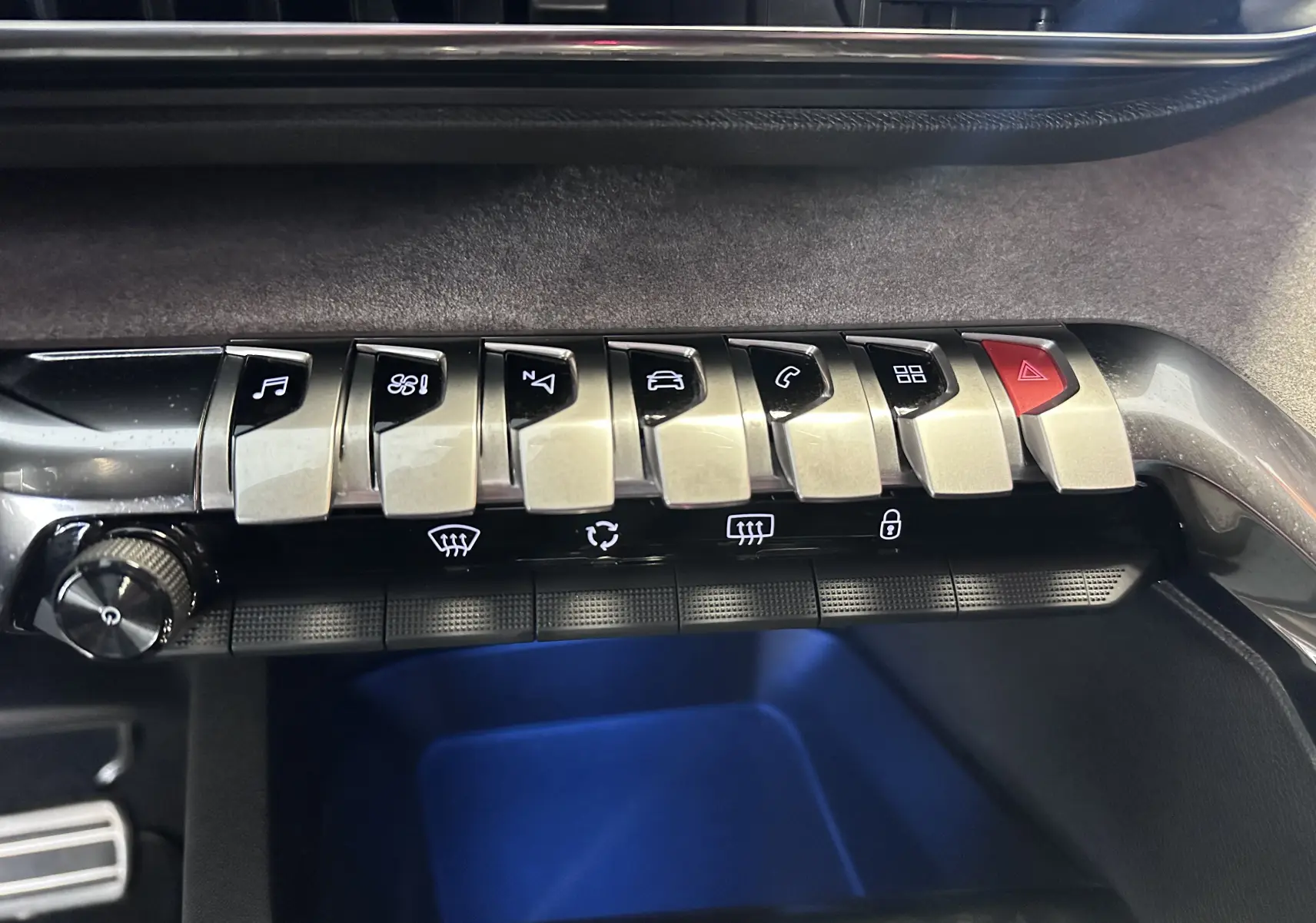 Gros plan sur la rangée de boutons argentés et noirs du tableau de bord du Peugeot 3008 blanc nacré, avec éclairage bleu dessous.