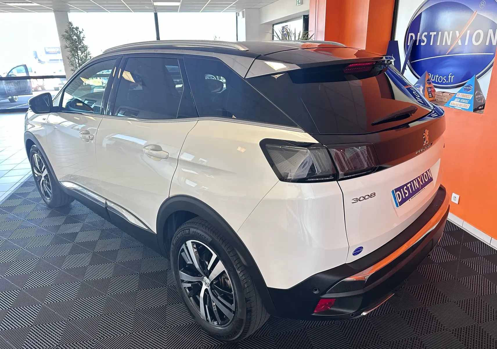 Vue 3/4 arrière droite d’un Peugeot 3008 blanc nacré avec toit noir et jantes alliage en showroom.