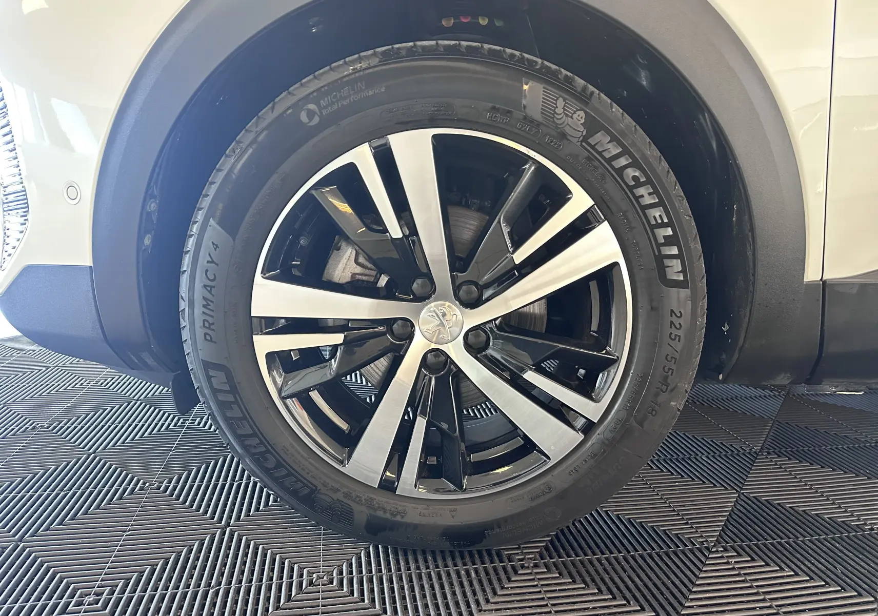 Gros plan sur la roue avant droite d’un Peugeot 3008 blanc nacré, jante alliage bicolore et pneu Michelin.