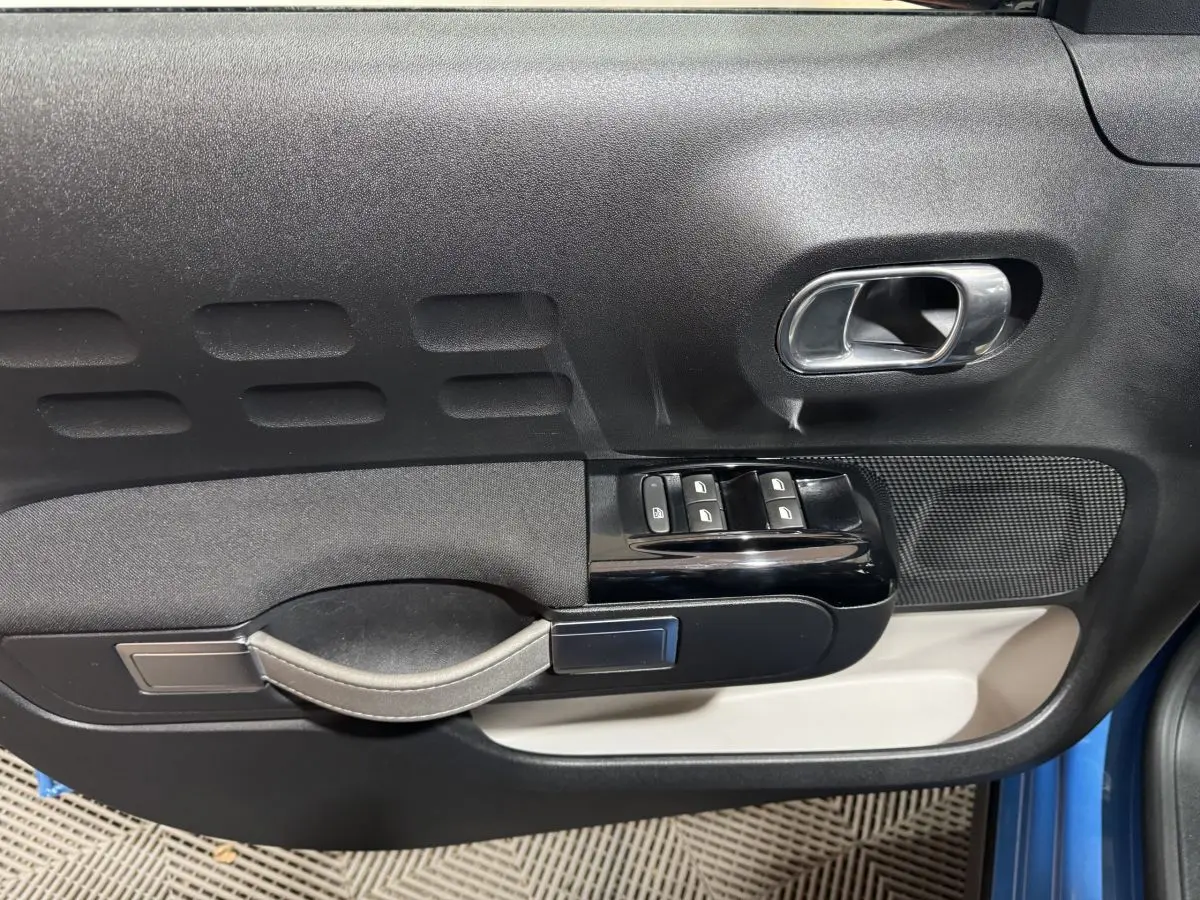 Vue rapprochée de la porte avant gauche de la Citroën C3 bleu, avec commandes de vitres et poignée intérieure chromée.