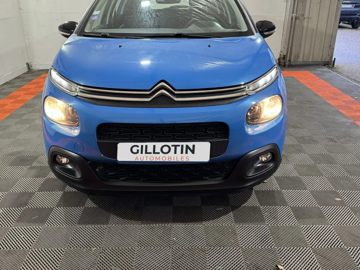 Vue avant d'une Citroën C3 bleu avec phares allumés et calandre noire dans un garage.