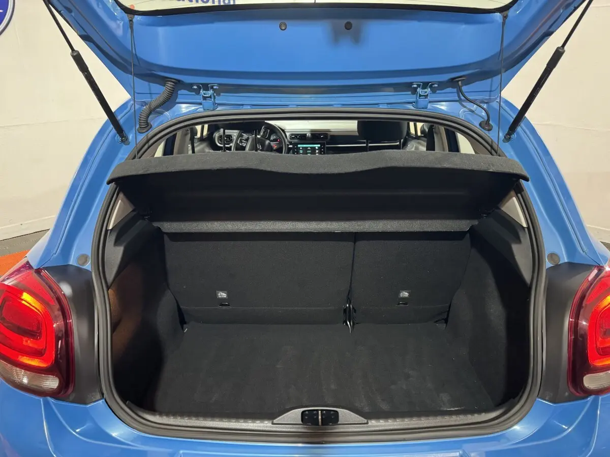 Vue arrière du coffre ouvert d'une Citroën C3 bleu 2018, montrant l'intérieur spacieux et la tablette de coffre relevée.