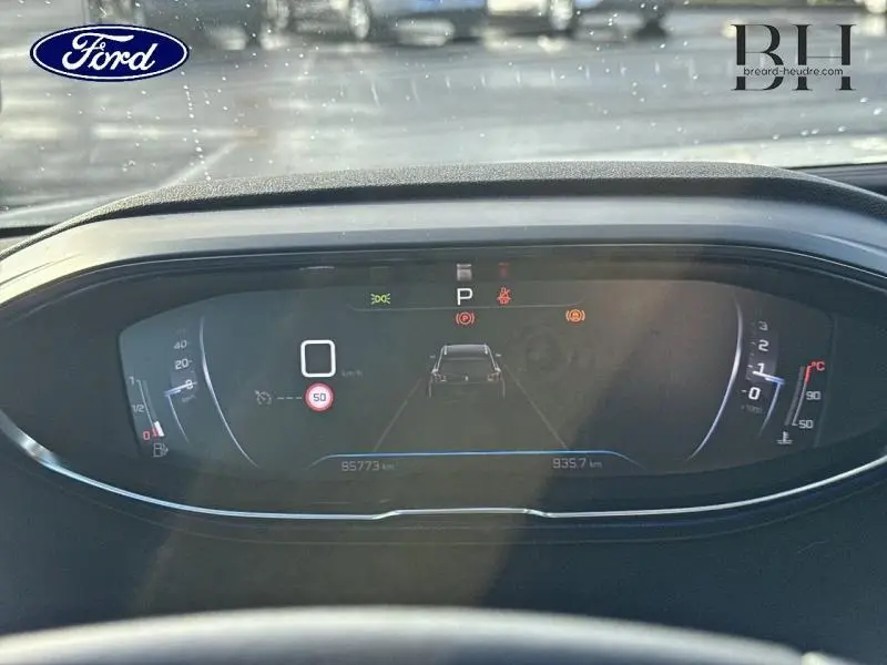 Affichage numérique du tableau de bord d'une Peugeot 5008 blanc banquise, avec indicateurs de vitesse et alertes visibles.