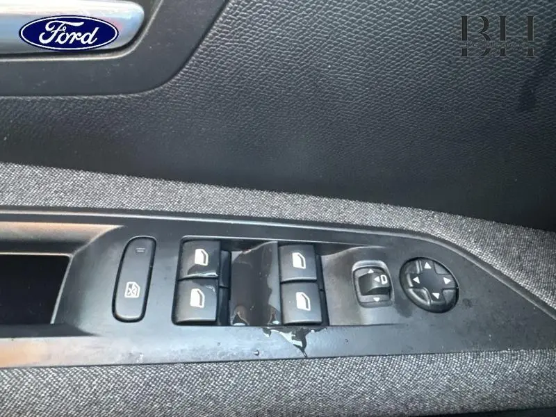 Panneau de commandes des vitres et rétroviseurs côté conducteur sur tissu gris, intérieur d'une voiture.