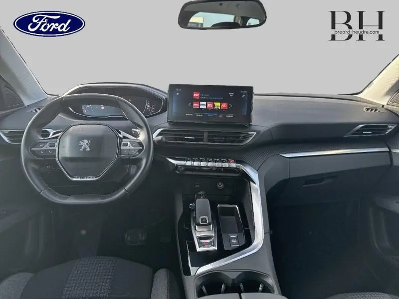 Vue intérieure avant du tableau de bord et volant cuir noir d’un Peugeot 5008 blanc Banquise avec écran tactile central.