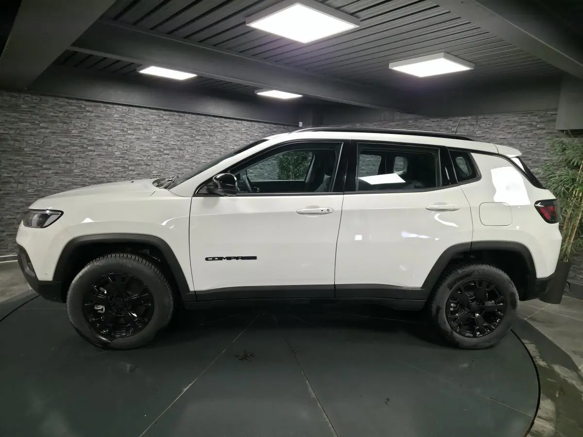 Vue de profil côté gauche d'un Jeep Compass blanc avec jantes noires et détails noirs contrastants en intérieur.