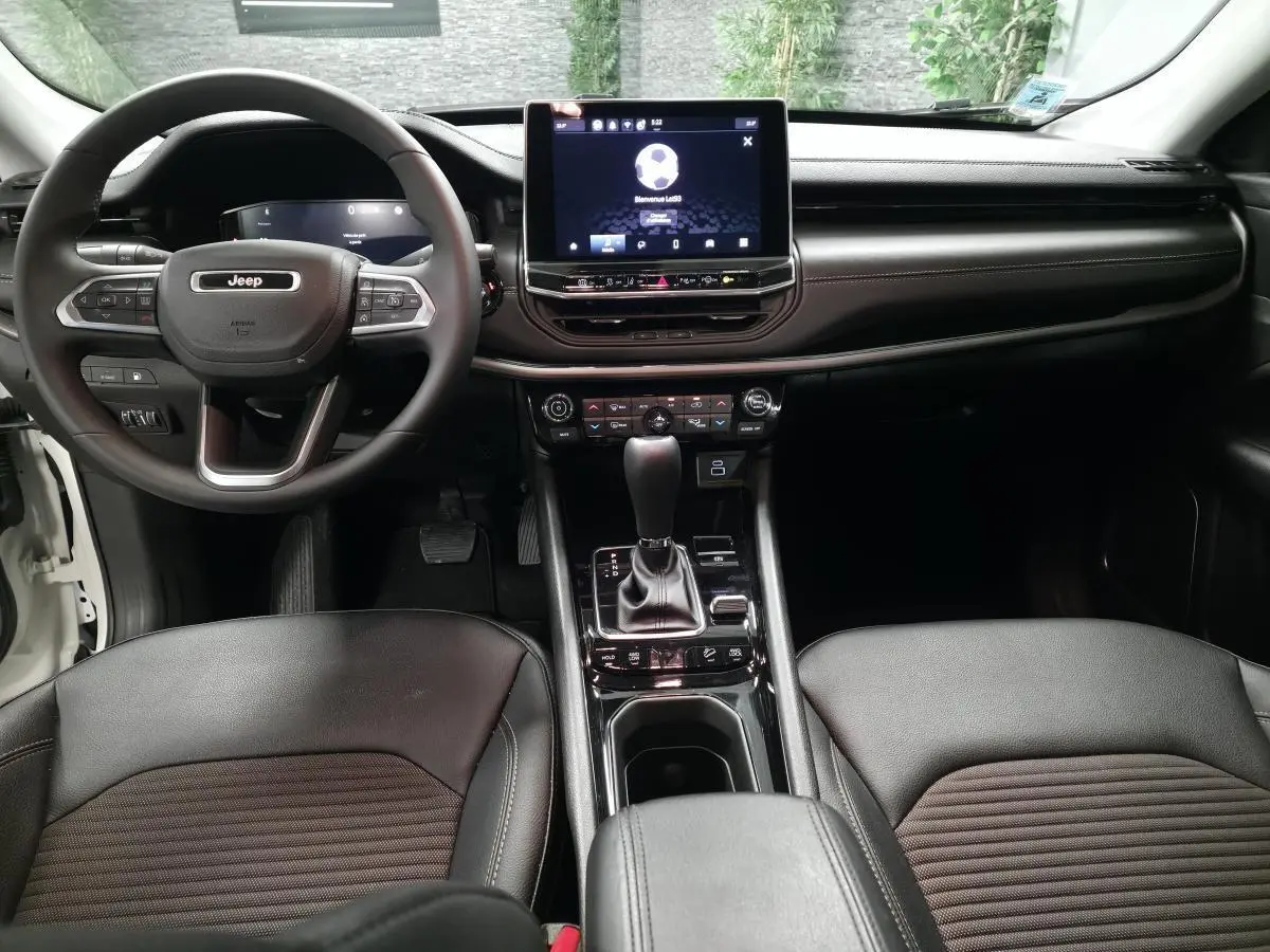 Vue intérieure avant du Jeep Compass 2024, tableau de bord noir avec écran tactile central et volant multifonction.