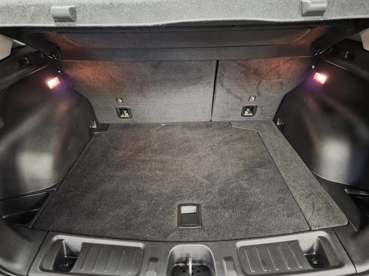 Coffre ouvert du Jeep Compass blanc 2024, vue intérieure montrant le tapis de sol et éclairage latéral.