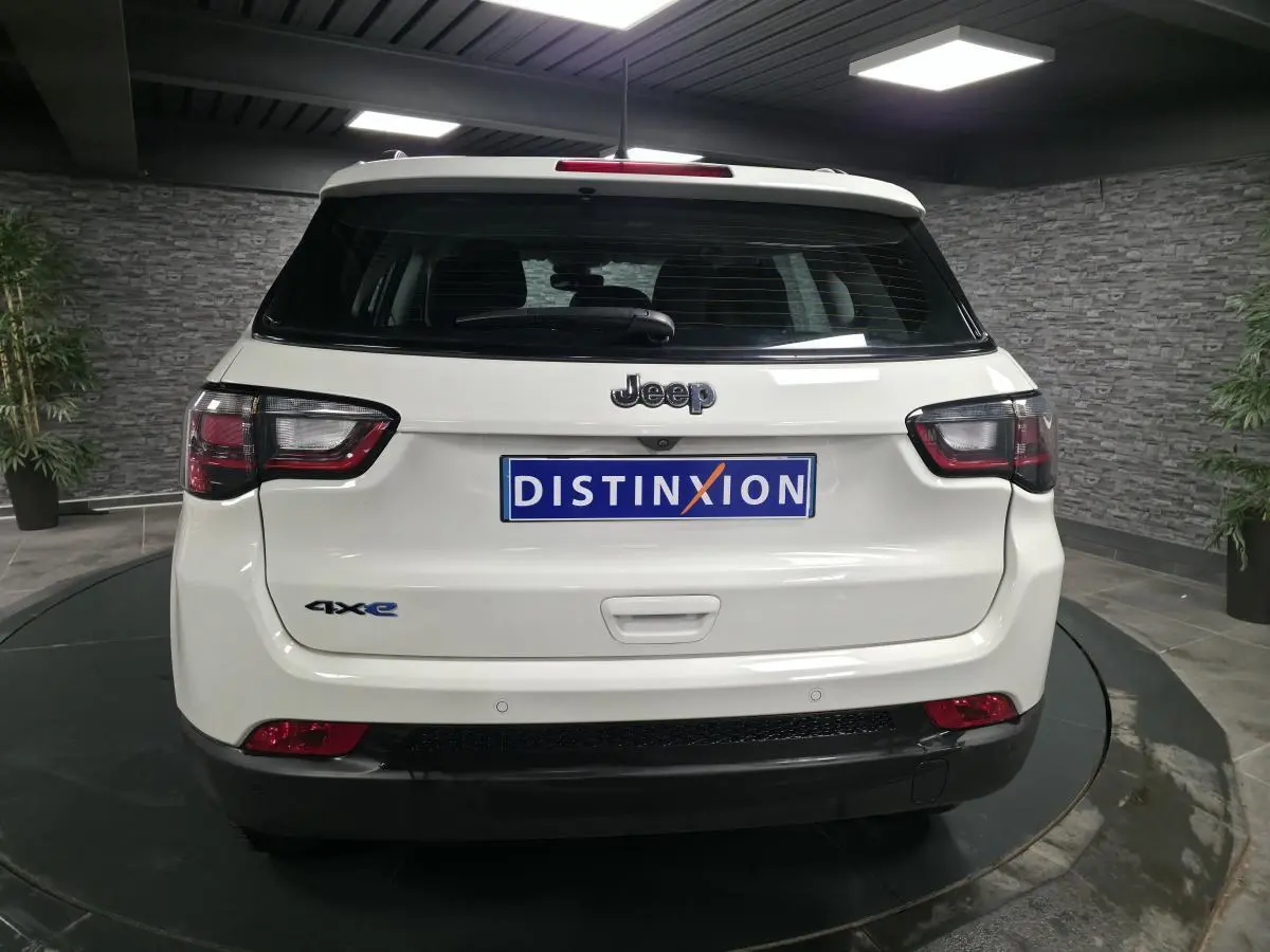 Vue arrière d’un Jeep Compass blanc hybride rechargeable avec logo 4xe et feux arrière LED dans un showroom.