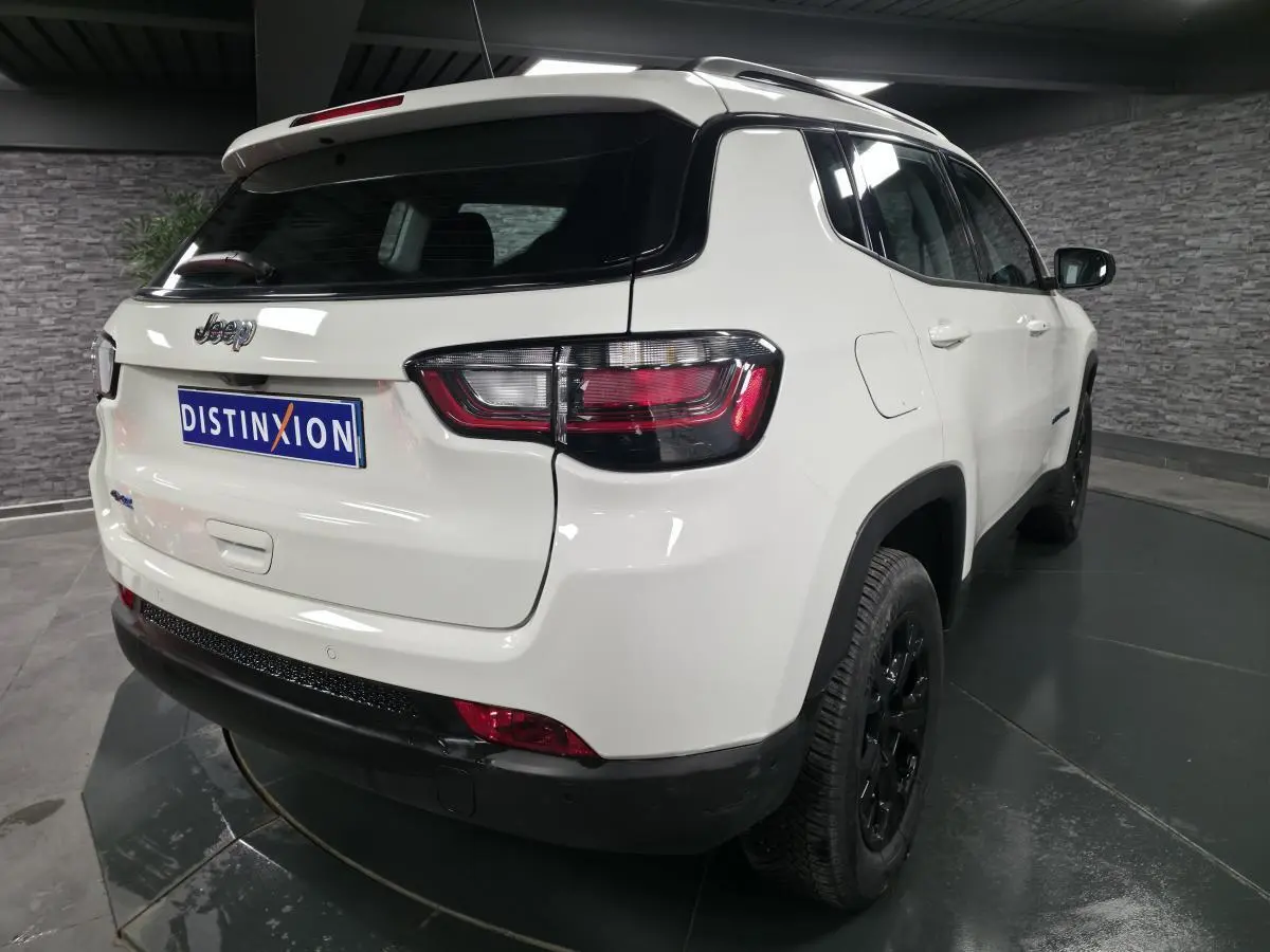 Vue 3/4 arrière droite d'un Jeep Compass blanc 2024 avec jantes noires et toit blanc en intérieur showroom.