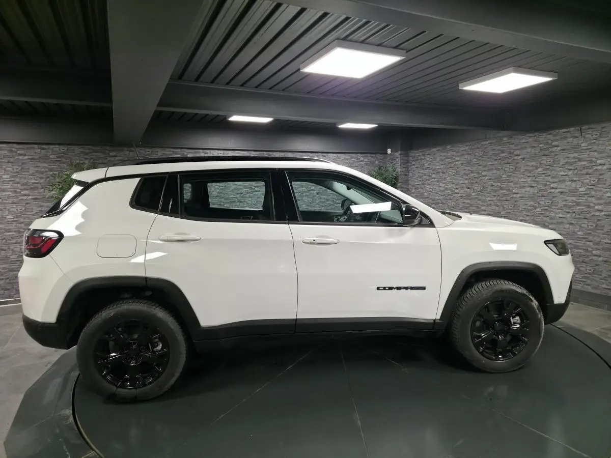 Jeep Compass blanc vu de profil côté gauche, avec jantes noires et toit noir dans un garage.