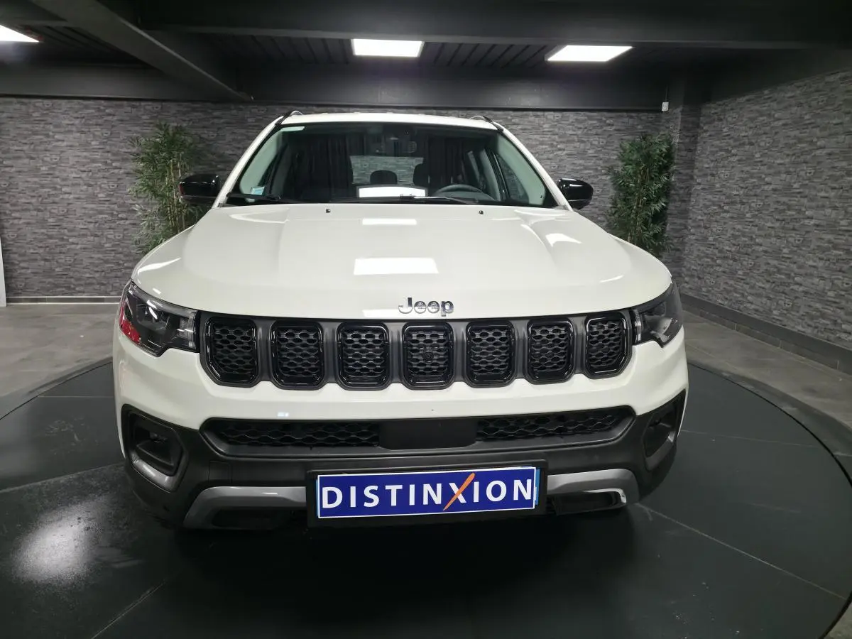 Vue frontale d'un Jeep Compass blanc avec calandre noire et logo Jeep visible sur fond intérieur gris.