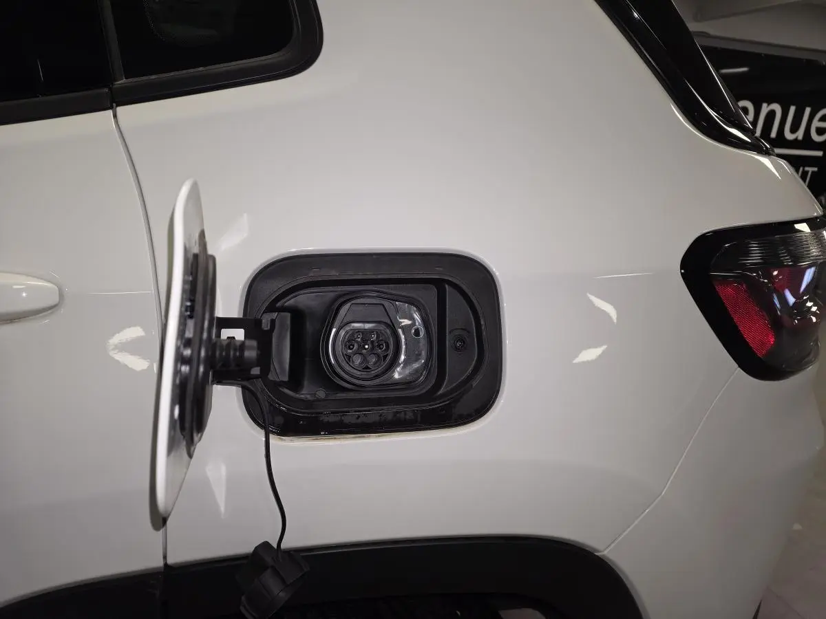 Prise de recharge ouverte côté gauche arrière d’un Jeep Compass blanc avec câble visible et feu arrière partiel.