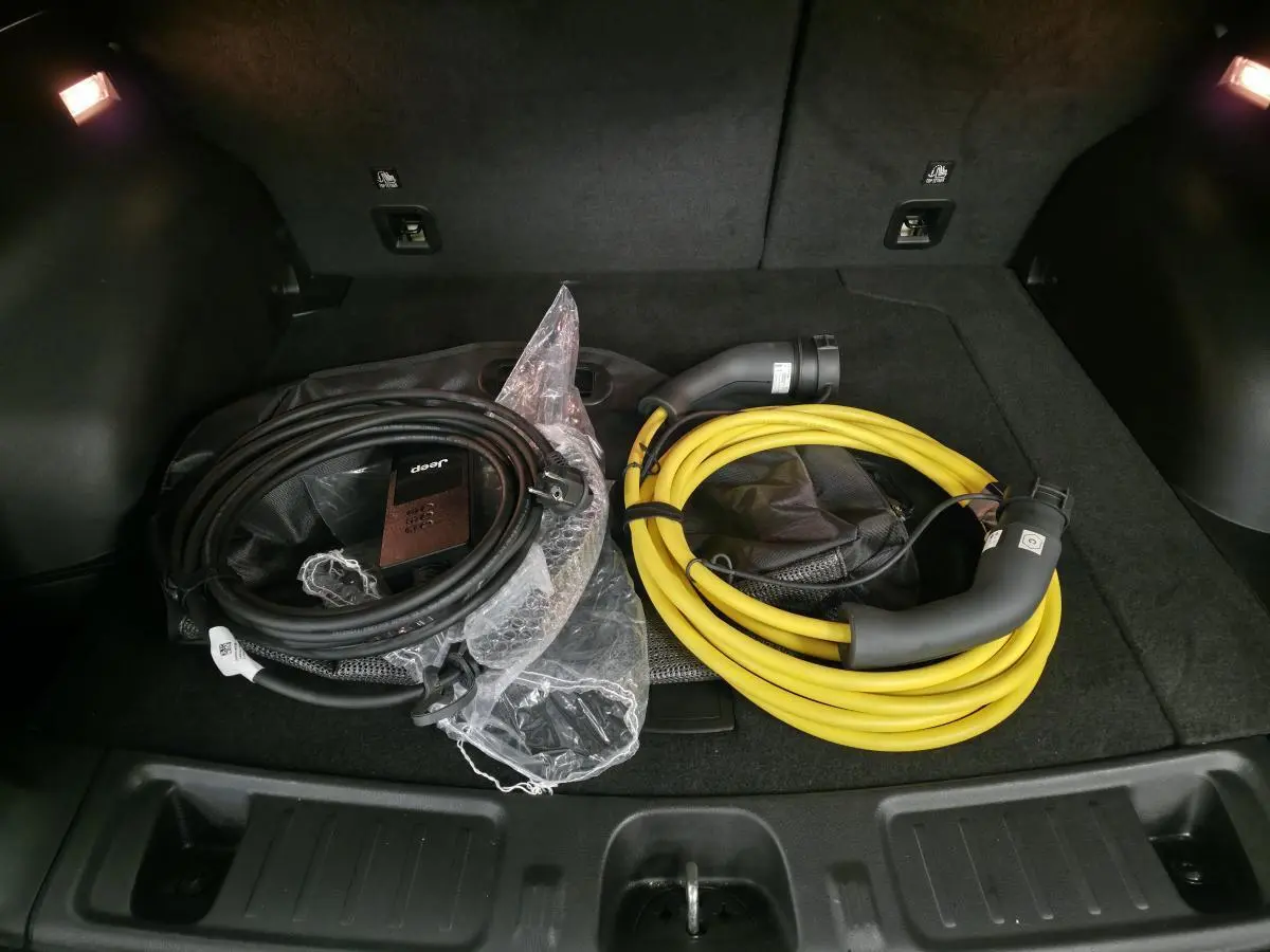 Vue du coffre du Jeep Compass 2024 avec câbles de recharge noir et jaune posés sur la moquette noire.