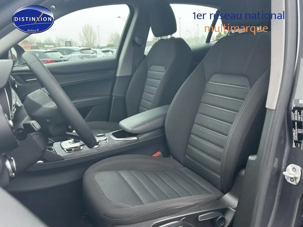 Vue intérieure côté conducteur de l'Alfa Romeo Stelvio gris Vesuvio, mettant en valeur les sièges et l'accoudoir central.