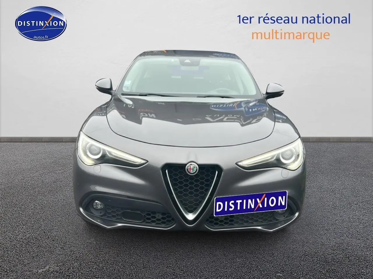Vue avant d'une Alfa Romeo Stelvio gris vesuvio metal avec phares allumés et calandre caractéristique en V.