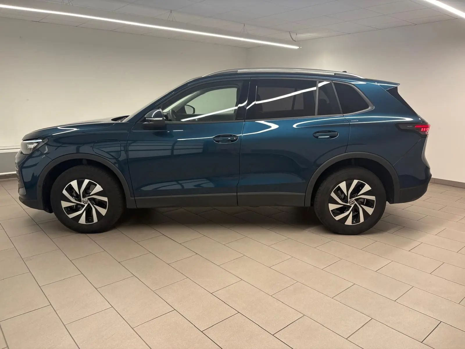 Vue de profil côté gauche du Volkswagen Tiguan 1.5 eHybrid TSI 204 DSG6 en bleu Nightshade métallisé, intérieur lumineux.