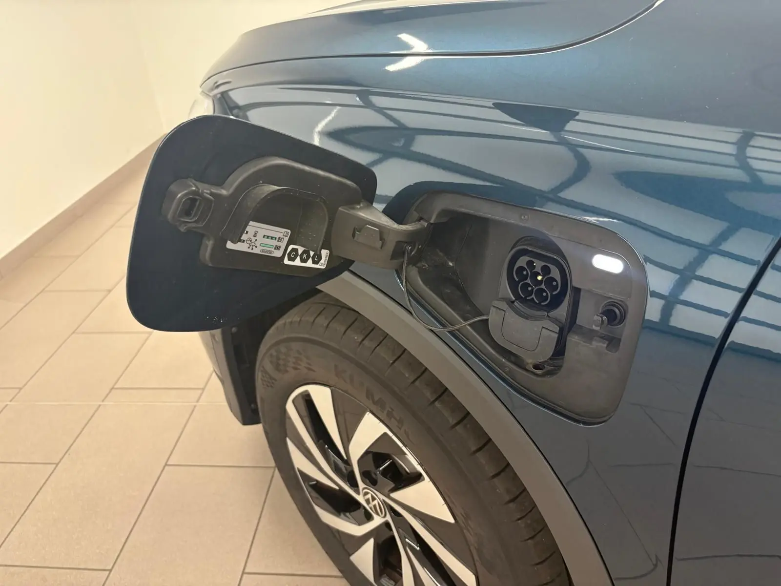 Prise de recharge ouverte côté gauche sur Volkswagen Tiguan 1.5 eHybrid TSI 204 Nightshade Blue, vue rapprochée sur la roue et la carrosserie.