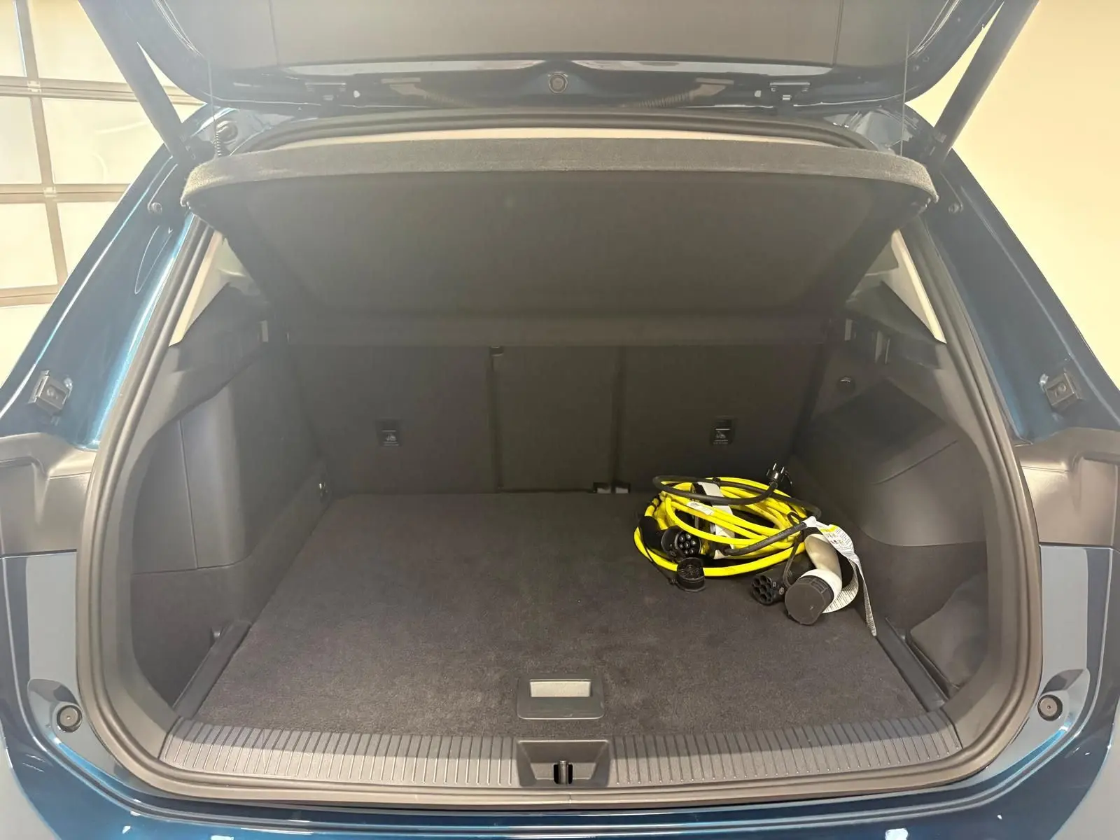 Coffre ouvert du Volkswagen Tiguan 1.5 eHybrid en Nightshade Blue, montrant un câble de recharge jaune dans un espace spacieux.