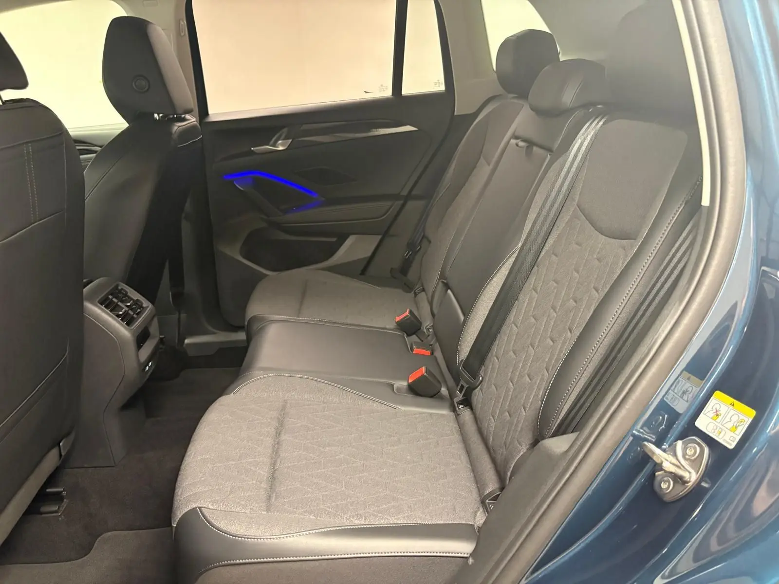 Vue intérieure côté droit des sièges arrière du Volkswagen Tiguan 1.5 eHybrid en Nightshade Blue avec éclairage d'ambiance bleu sur la portière.