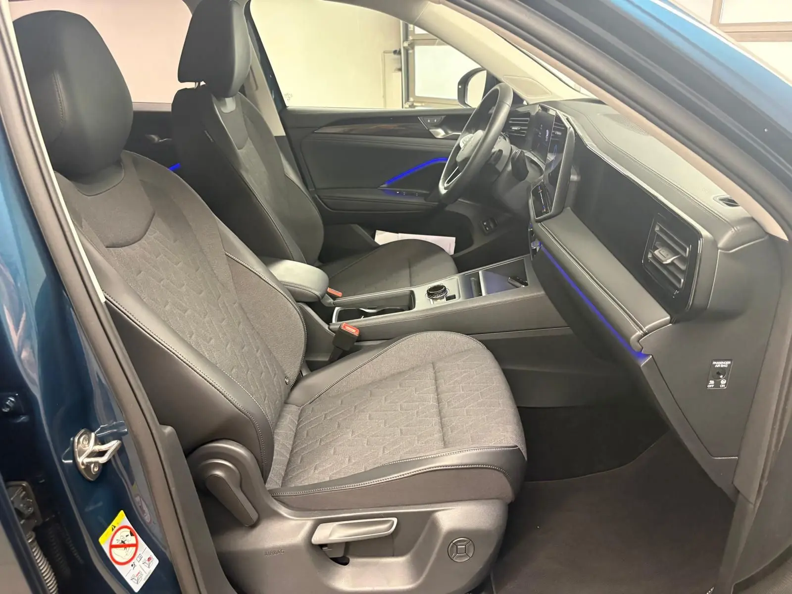 Intérieur avant droit du Volkswagen Tiguan 1.5 eHybrid Nightshade Blue avec sièges chauffants et éclairage d'ambiance bleu.