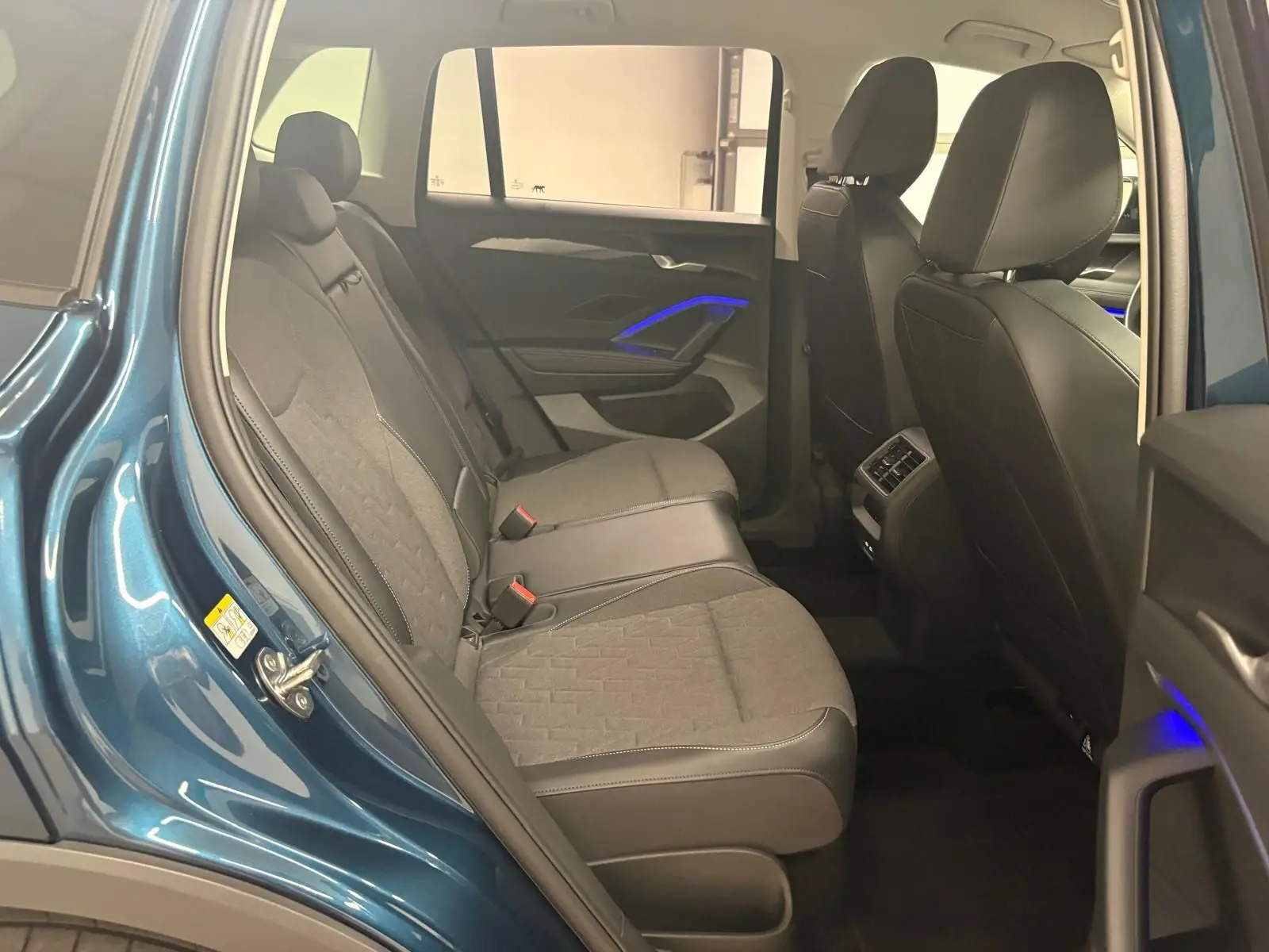 Vue intérieure arrière droite du Volkswagen Tiguan 2025 Nightshade Blue, sièges tissu et cuir, éclairage d'ambiance bleu sur les portes.