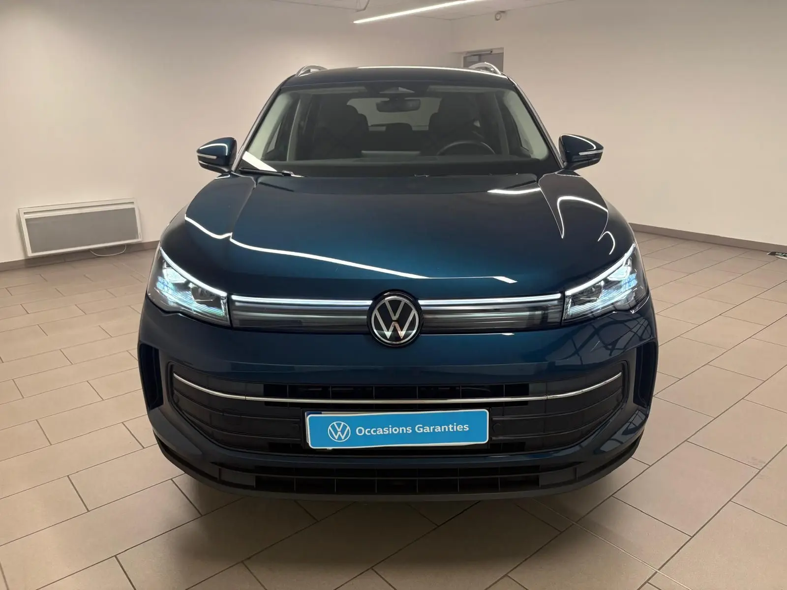 Vue frontale du Volkswagen Tiguan 1.5 eHybrid TSI 204 DSG6 en bleu Nightshade, avec phares LED allumés dans un showroom.