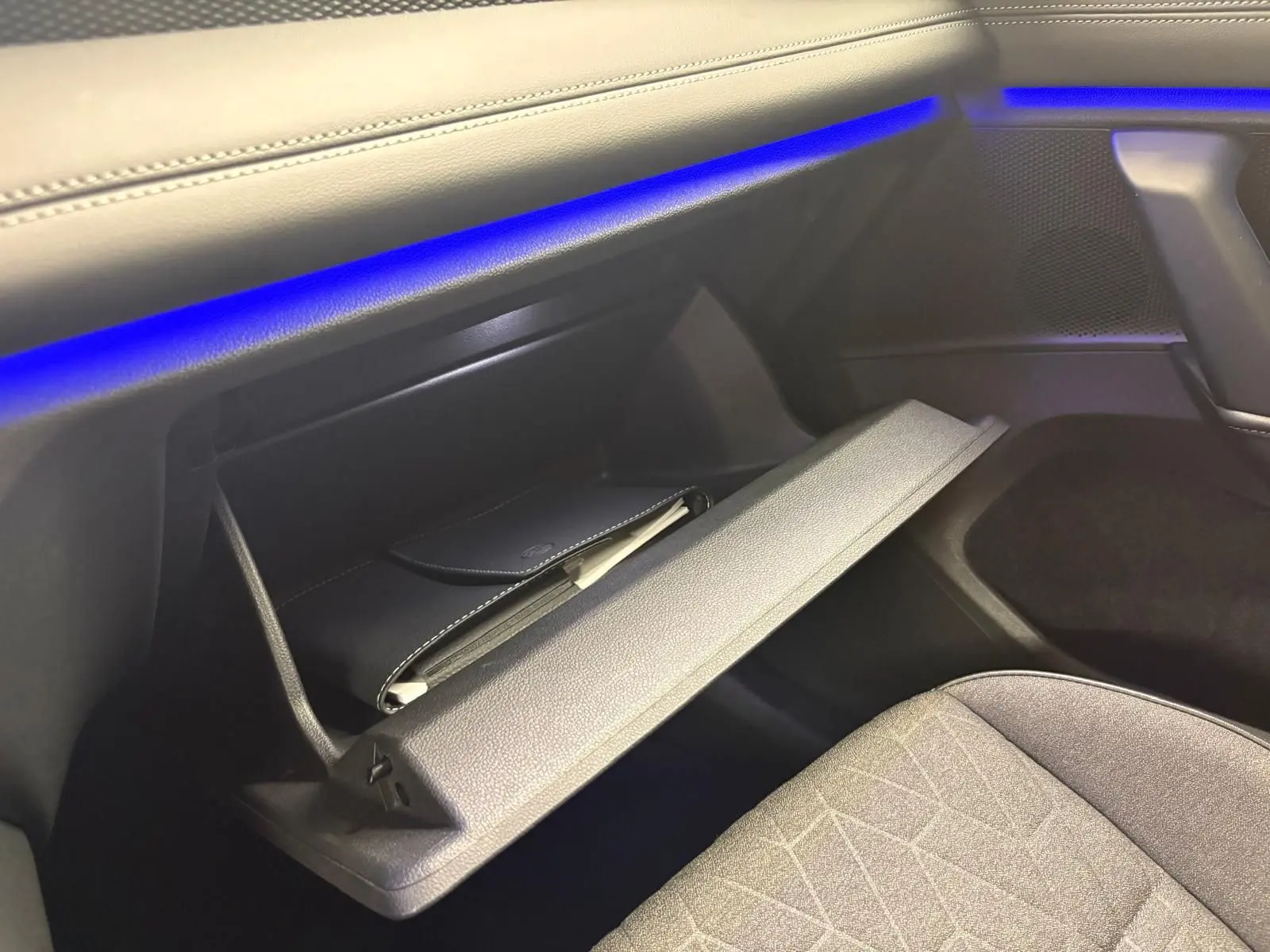 Gant de boîte à gants ouvert côté passager avec éclairage d'ambiance bleu sur tableau de bord du Volkswagen Tiguan 2025.
