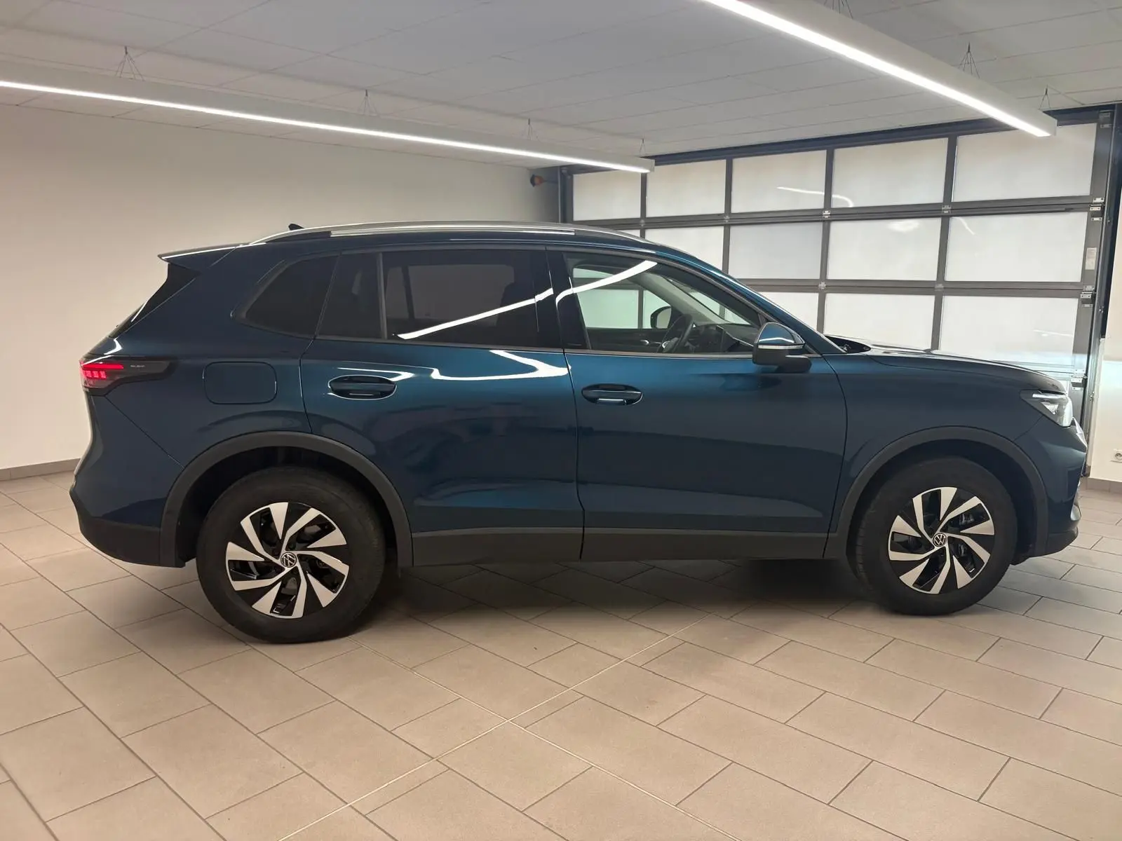 Vue de profil côté gauche du Volkswagen Tiguan 1.5 eHybrid TSI 204 DSG6 en bleu métallisé Nightshade, intérieur visible par les vitres teintées.