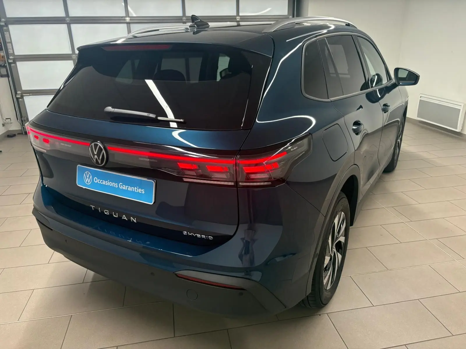 Vue 3/4 arrière droite du Volkswagen Tiguan 1.5 eHybrid TSI 204 DSG6 en bleu Nightshade, avec feux arrière allumés.