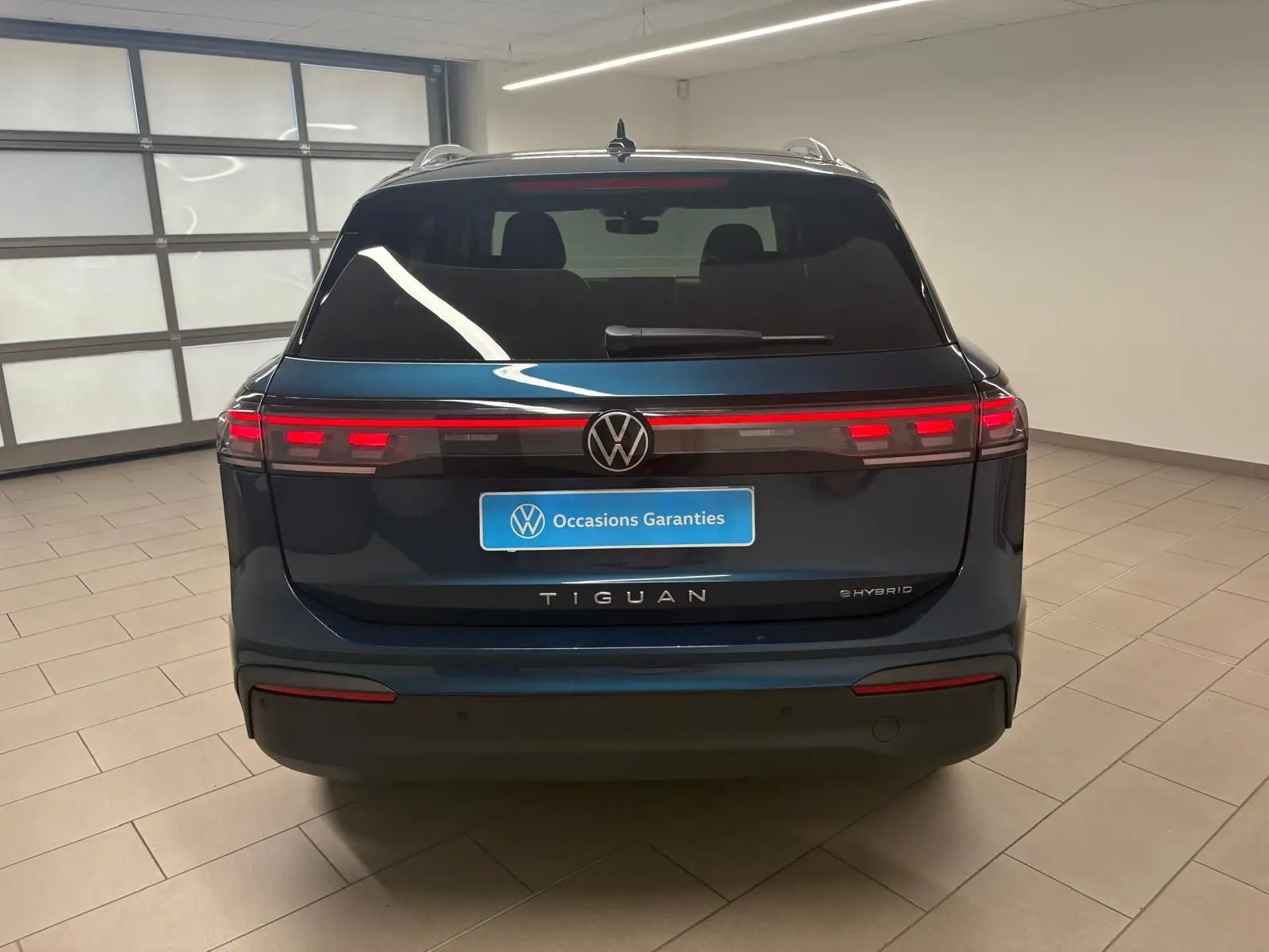 Vue arrière du Volkswagen Tiguan hybride rechargeable 2025 en Nightshade Blue, avec feux arrière LED allumés dans un garage.