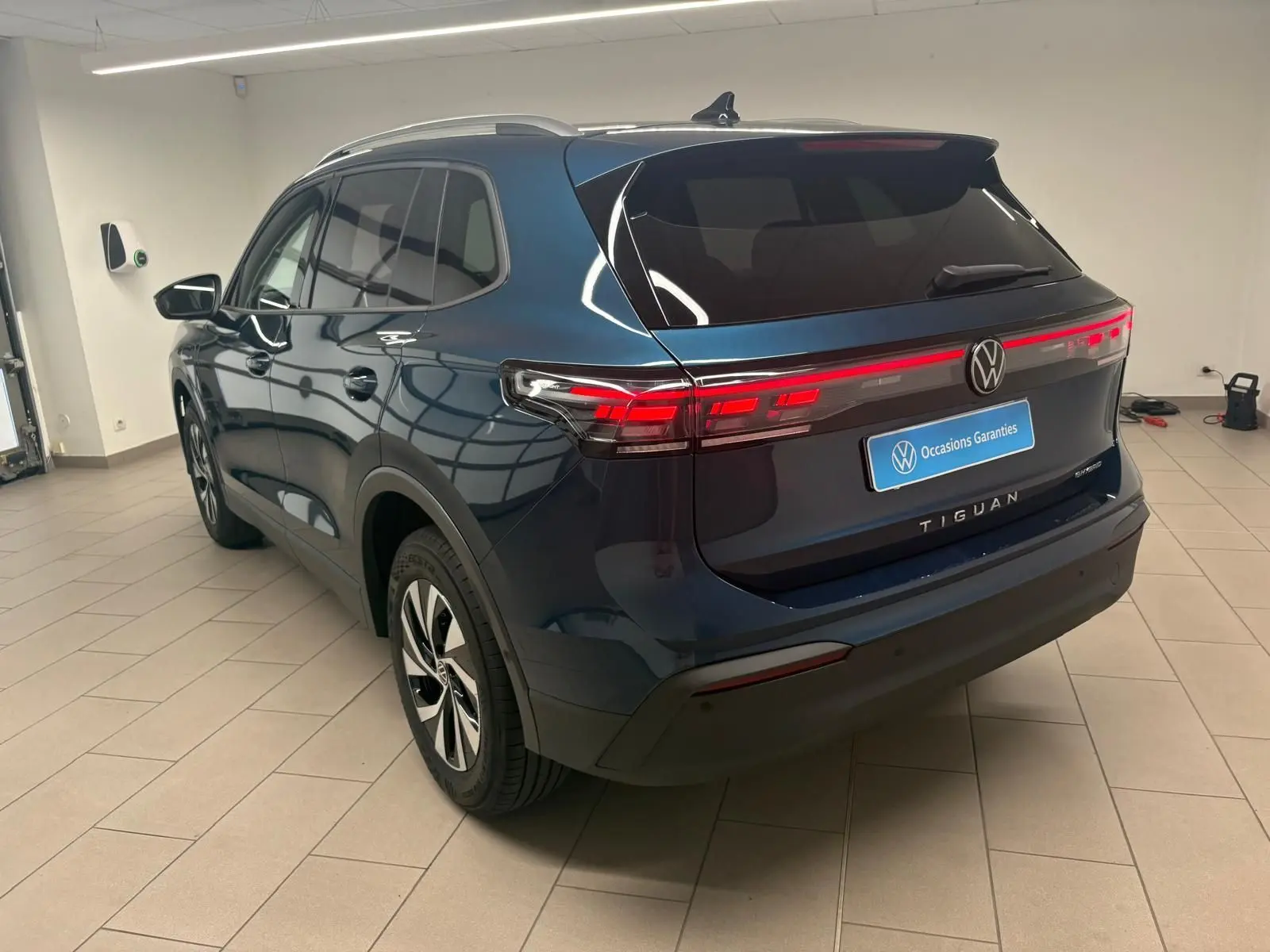 Vue 3/4 arrière droite du Volkswagen Tiguan 1.5 eHybrid TSI 204 DSG6 en bleu Nightshade, avec feux arrière allumés.